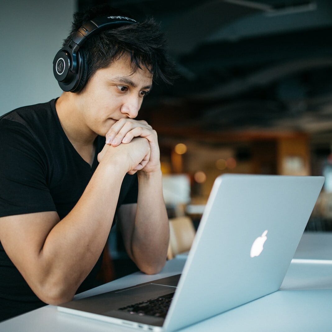 man wearing headphones while sitting on chair in front of MacBook